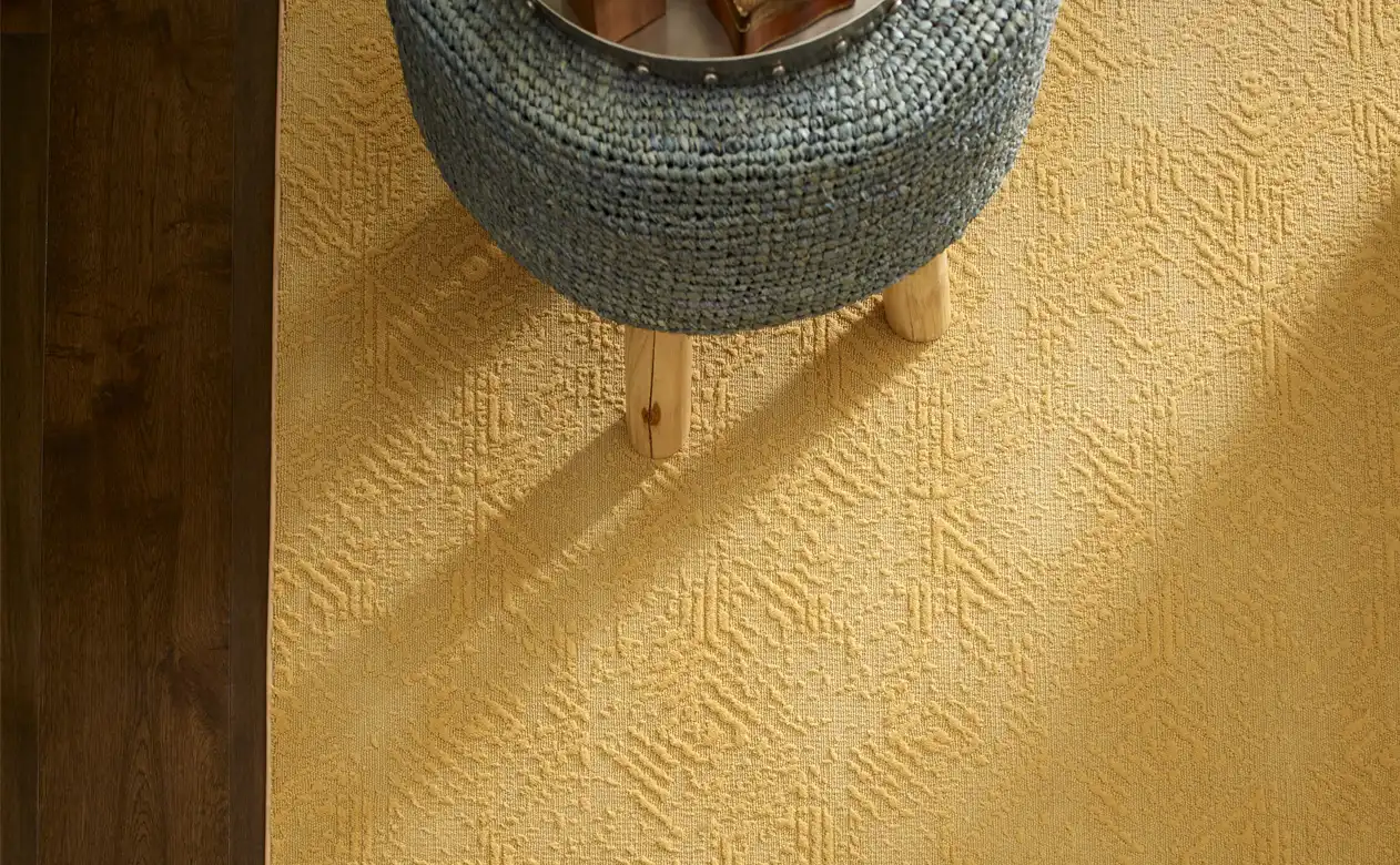 yellow area rug with motif pattern on dark wood flooring with grey stool